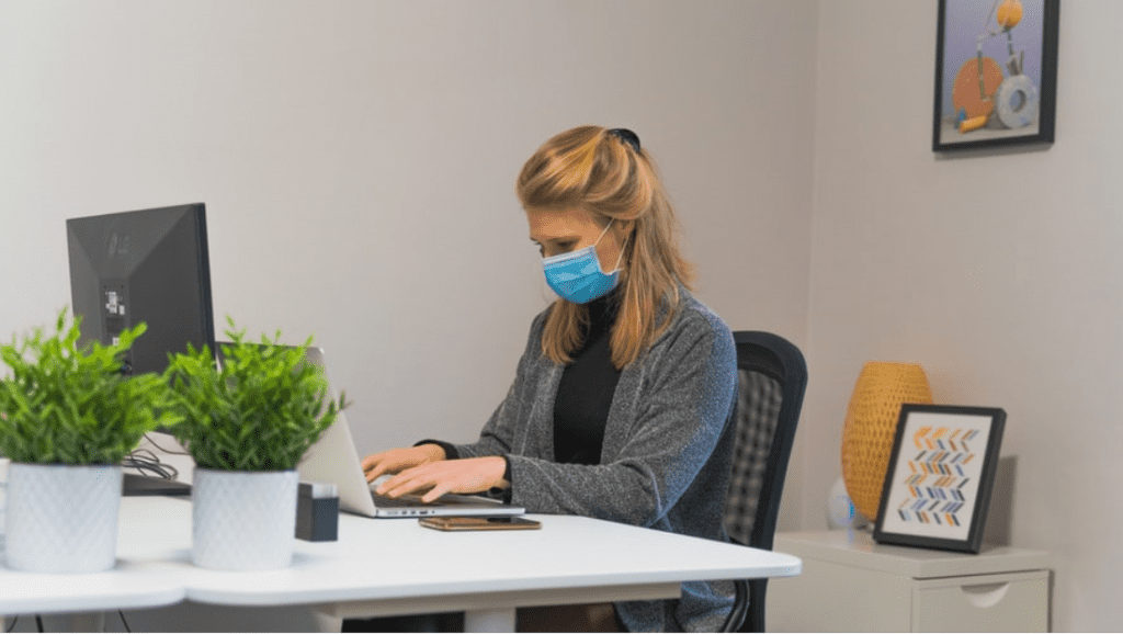 Eine junge Frau arbeitet in ihrem Büro und trägt eine chirurgische Maske. 